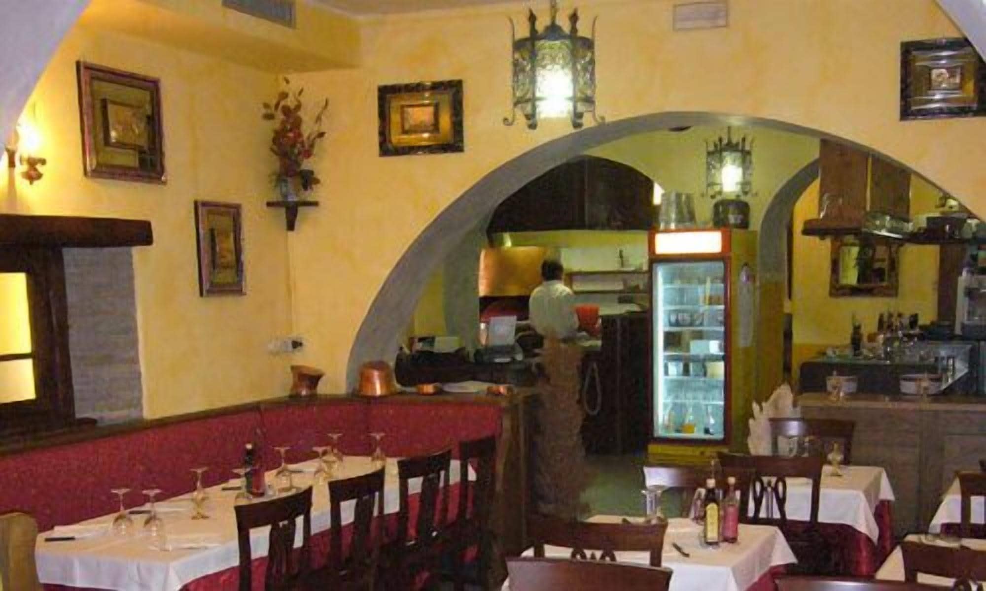 Ein Restaurant mit gedeckten Tischen, einer Bar und einer durch einen Bogen einsehbaren Küche.