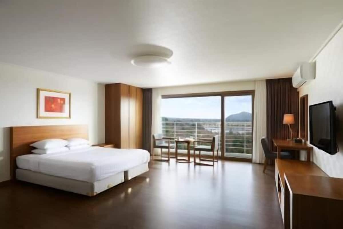 Quarto de hotel com cama, escrivaninha com cadeira, televisão e varanda com vista.