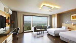 Habitación de hotel con dos camas, un escritorio, una silla, un televisor y un amplio ventanal con vistas.