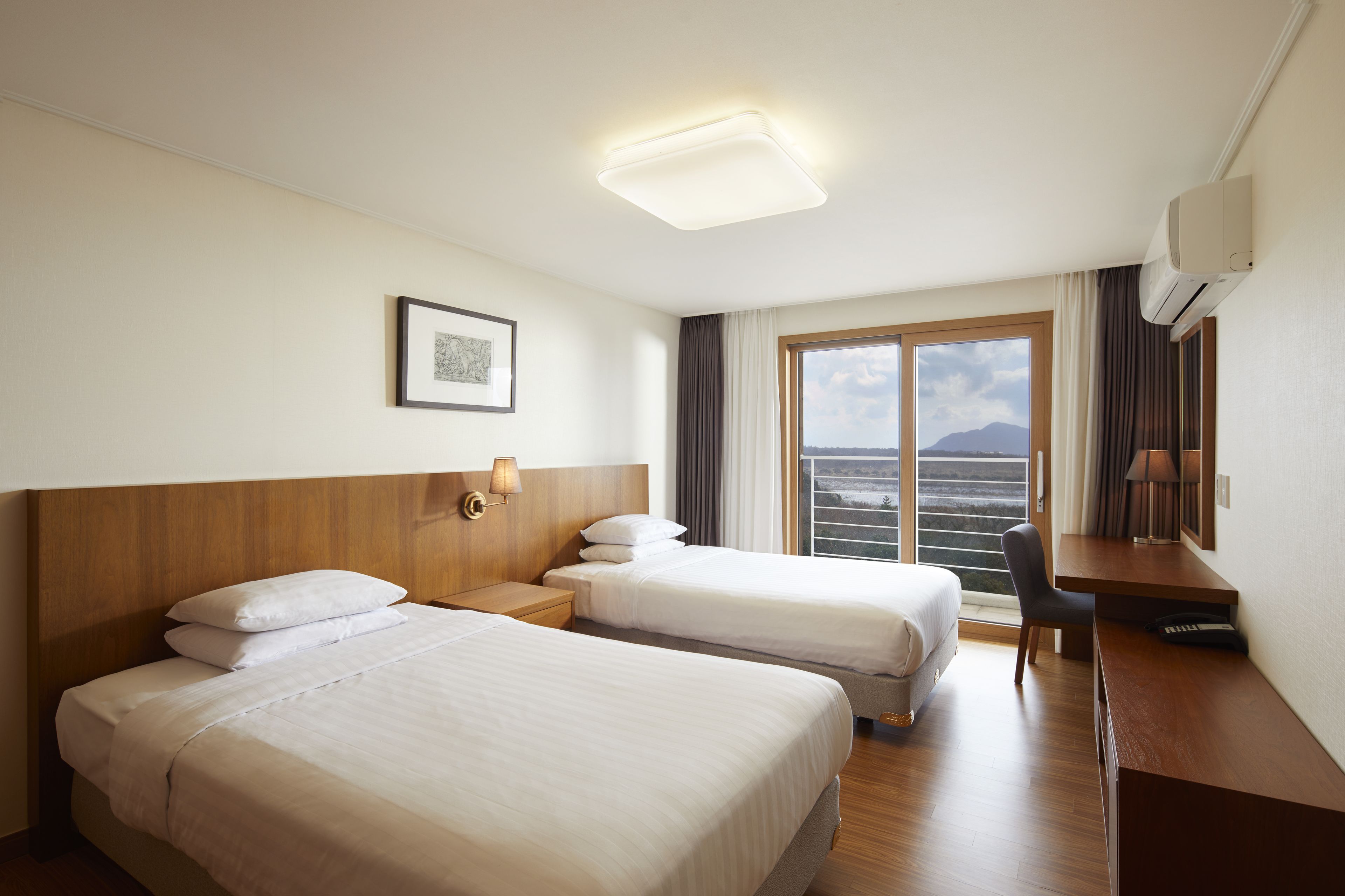 Une chambre d’hôtel avec deux lits, un bureau, une chaise, un tableau encadré au mur et une grande fenêtre donnant sur la mer.