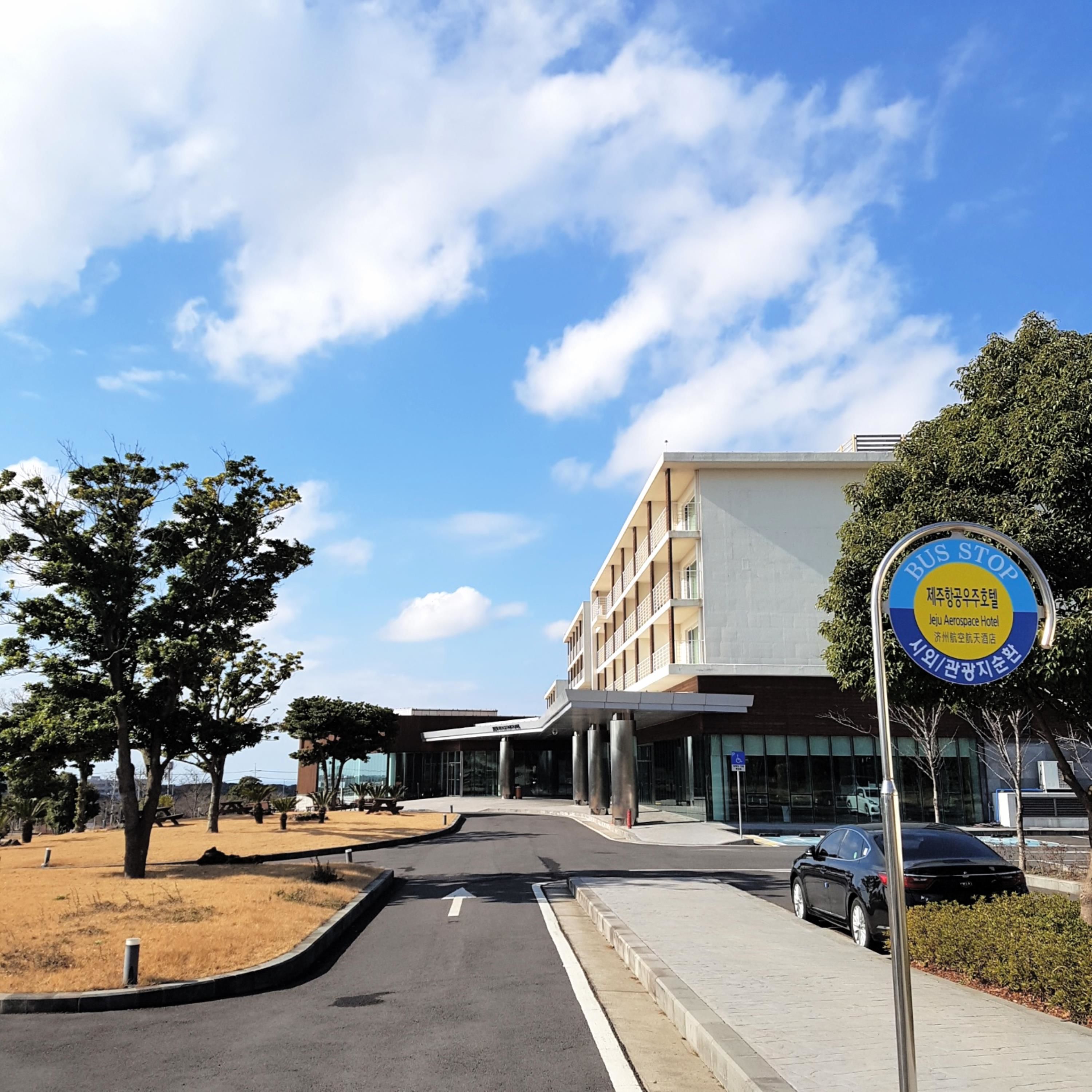 Ein modernes Gebäude mit einem Bushaltestellen-Schild, einem Parkplatz und blauem Himmel.
