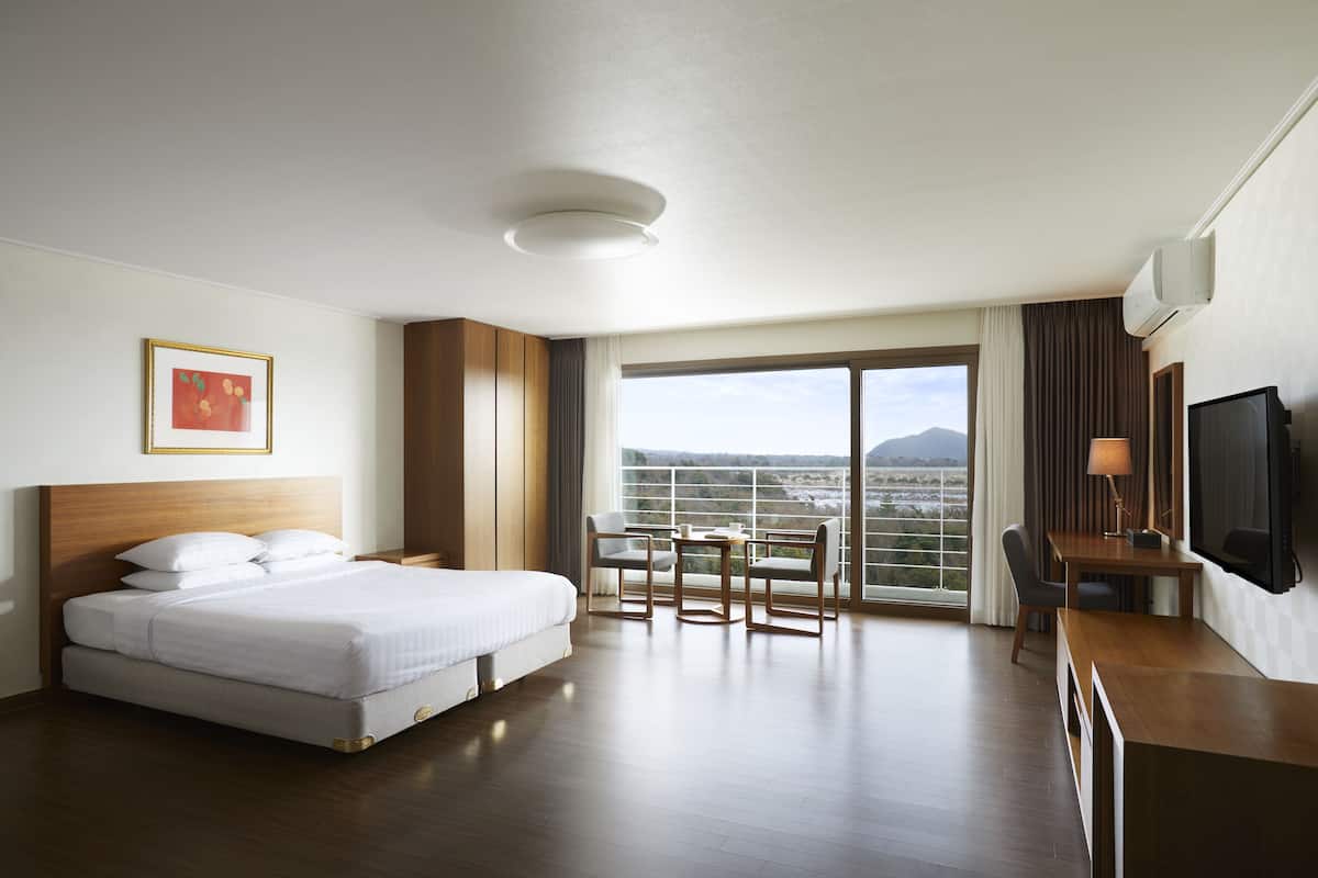 Quarto de hotel com uma cama grande, uma escrivaninha com cadeira, televisão e varanda com vista.