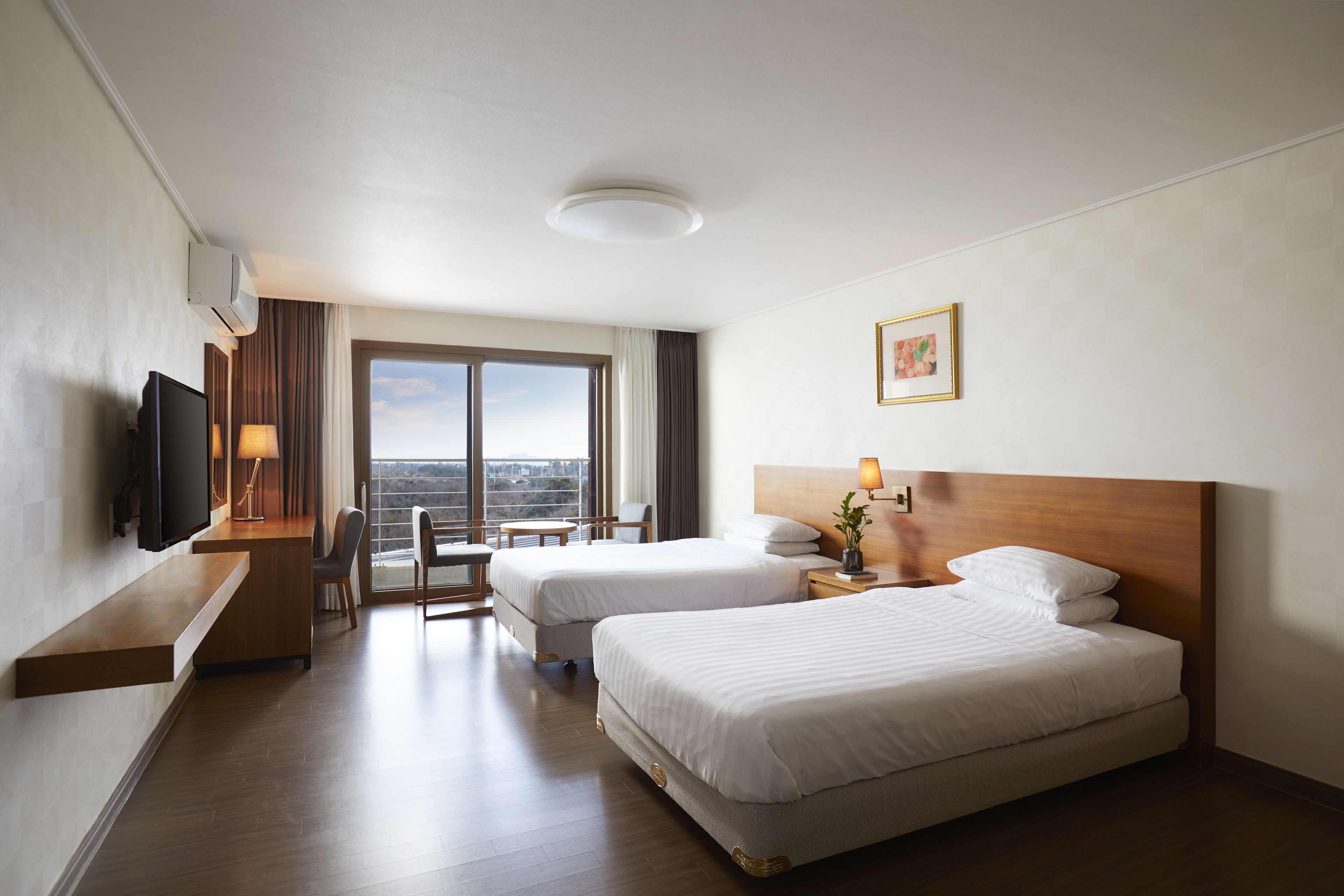 A hotel room with two beds, a TV, a desk, and a window with a city view.