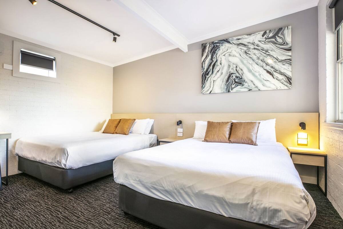 A hotel room with two beds, a marble wall art, a window, and a nightstand with a lamp.