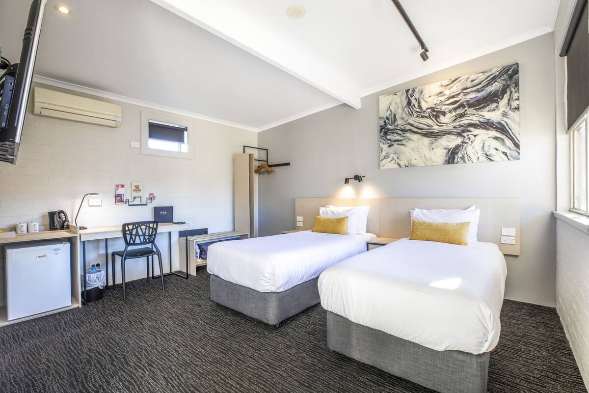 A hotel room with two beds, a desk, a chair, and a large abstract painting on the wall.
