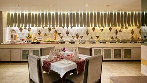 A buffet setup with multiple serving stations, a central dining area with tables set for two, and a decorative wall with geometric patterns. - Sapna Clarks Inn (Lucknow)