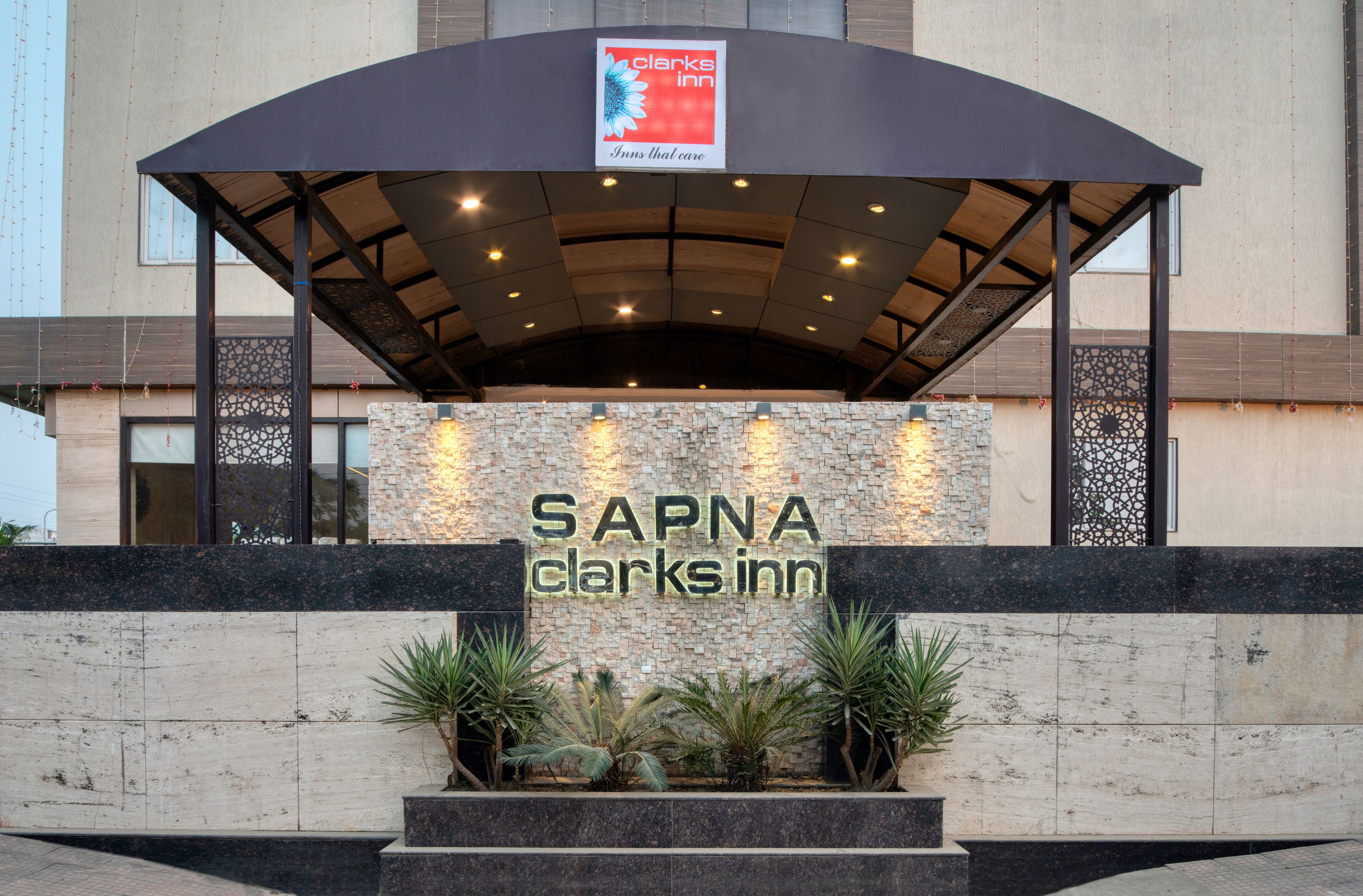 The exterior of SAPNA Clark's Inn with a covered entrance, stone facade, and decorative plants.