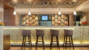 A bar area with three stools, a television, and shelves with bottles and vases. - Sapna Clarks Inn (Lucknow)