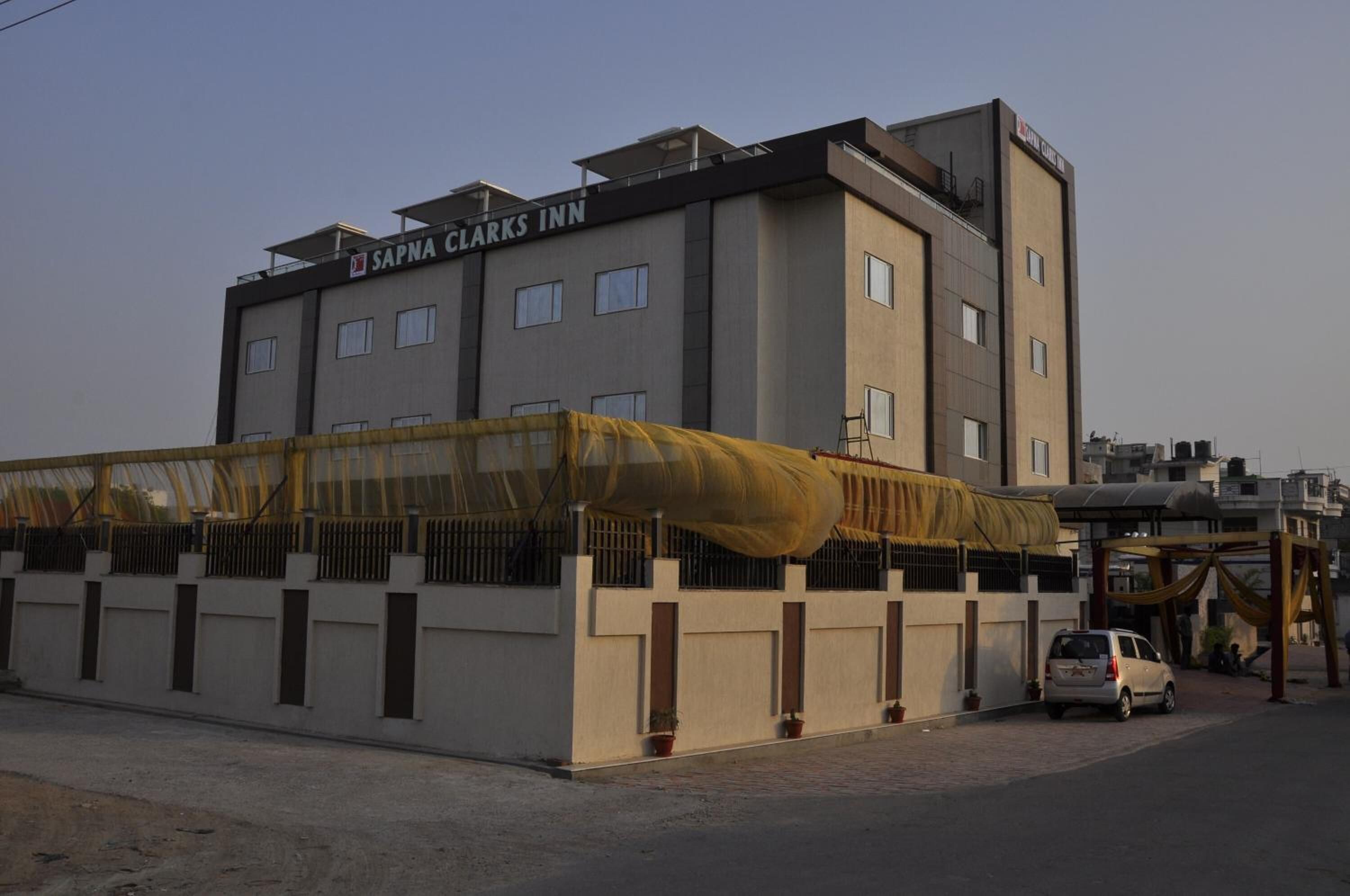 A multi-story hotel named SAPNA CLARKS INN with a modern design, featuring a covered entrance area and a visible car parked in front.