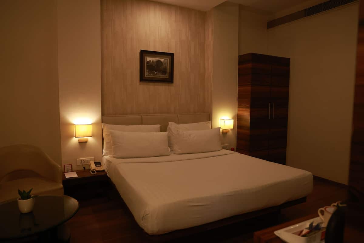 Une chambre d’hôtel avec un grand lit, des lampes de chevet, une petite table avec une plante, une table de chevet et une armoire.