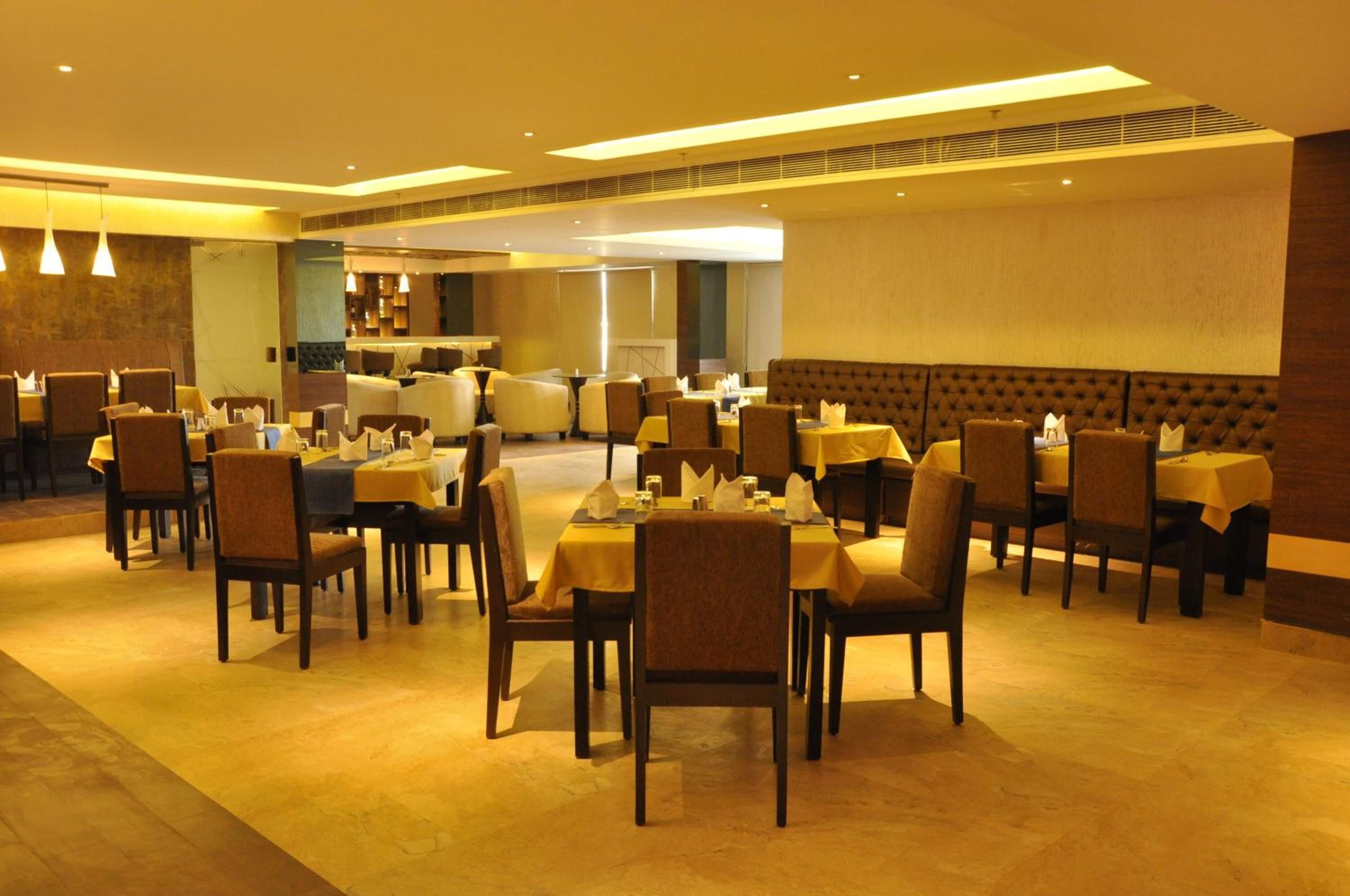 Un restaurant doté de nombreuses tables et chaises, d’un plafond haut avec des luminaires encastrés et d’un aménagement intérieur moderne.