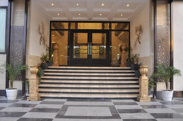 A hotel entrance with a grand double door, steps leading up to it, and decorative columns on either side.