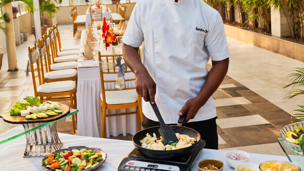 A chef preparing food outdoors with a buffet setup, including various dishes and cooking equipment. - Sapna Clarks Inn (Lucknow)