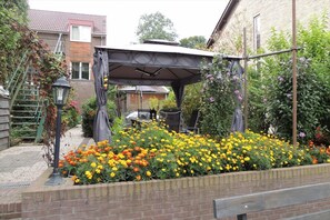 A garden with a brick wall, yellow and orange flowers, and a pergola structure. - Pension de Dael (Valkenburg aan de Geul)