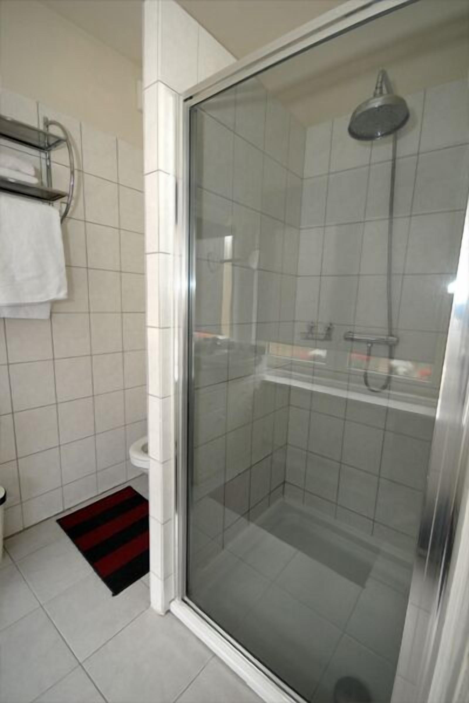 A modern bathroom with a glass-enclosed shower, a white toilet, and a red and black striped rug.