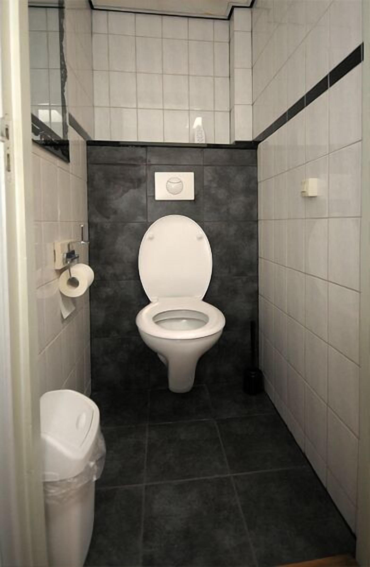 A small, compact bathroom with a white toilet, a trash bin, and a toilet paper holder on the wall.
