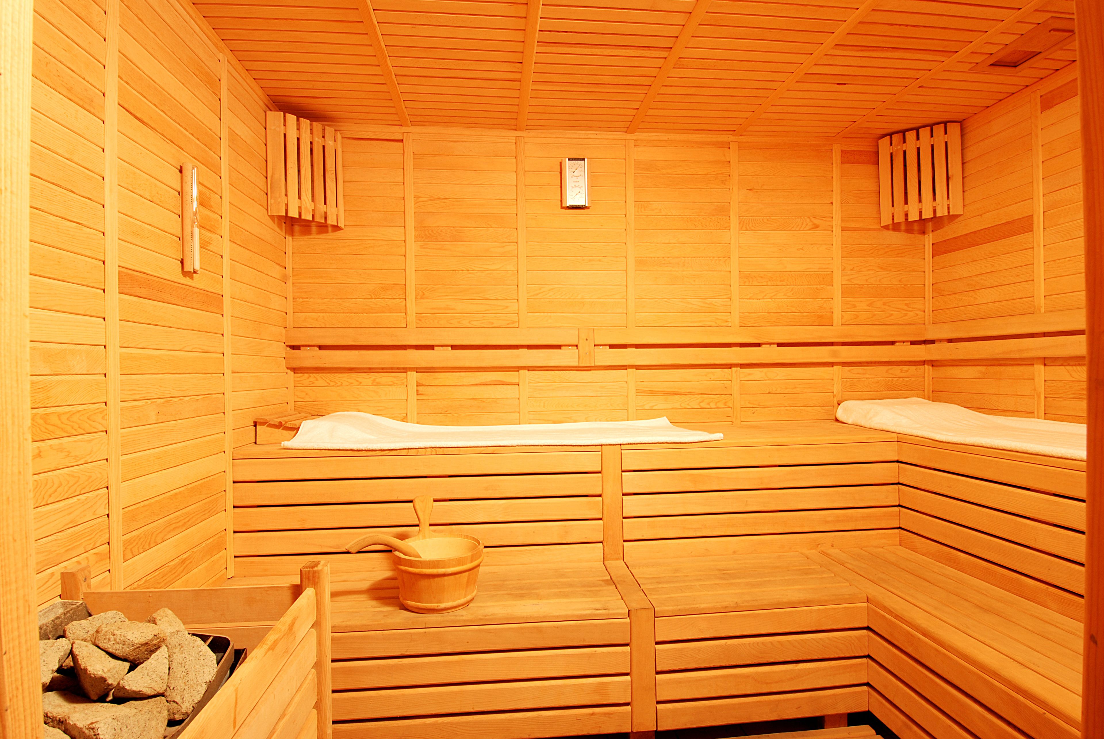 A sauna with wooden benches, a bench heater, and a bucket of stones.