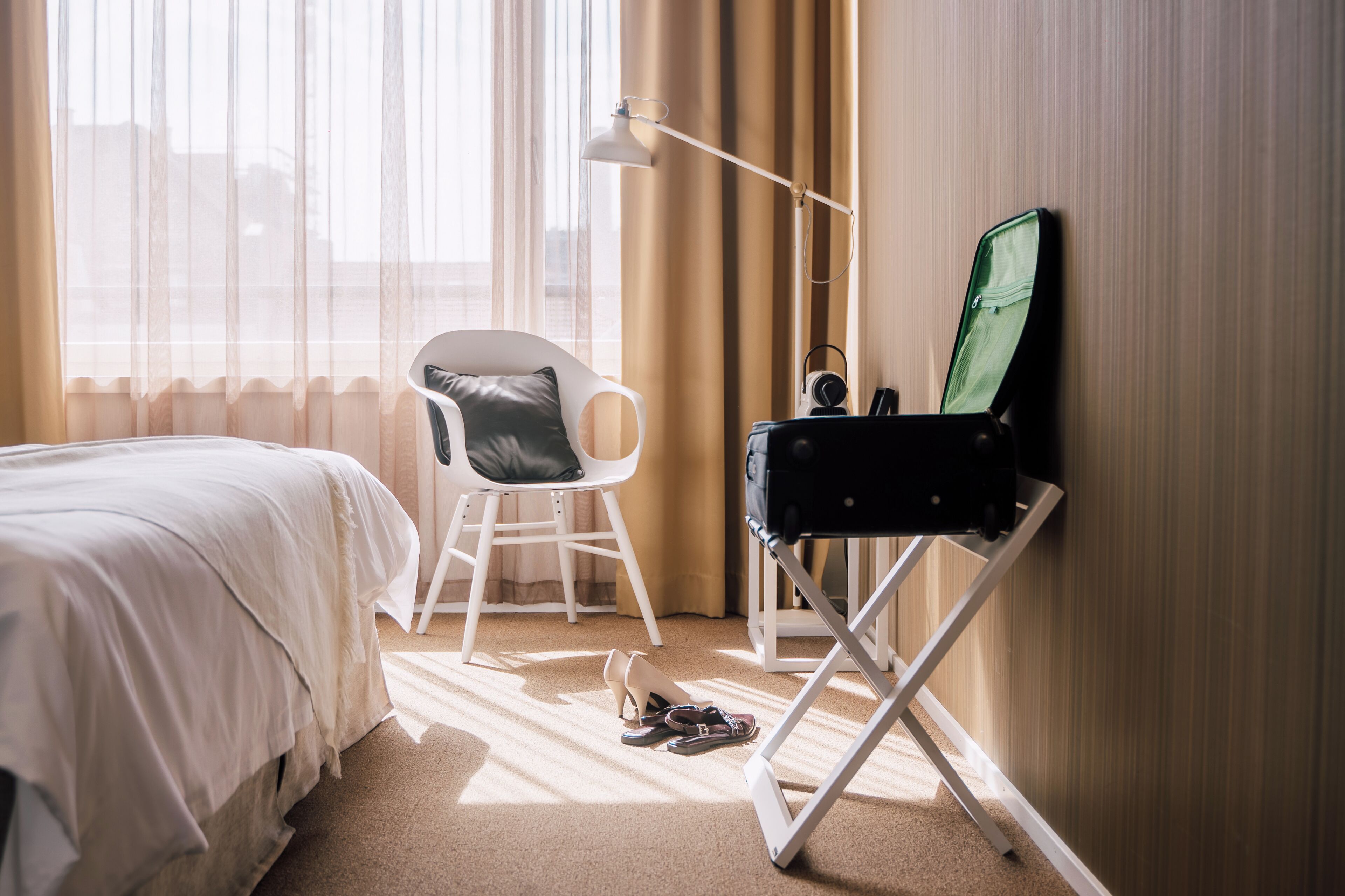 A hotel room with a bed, a chair, a desk, and a large window with curtains.