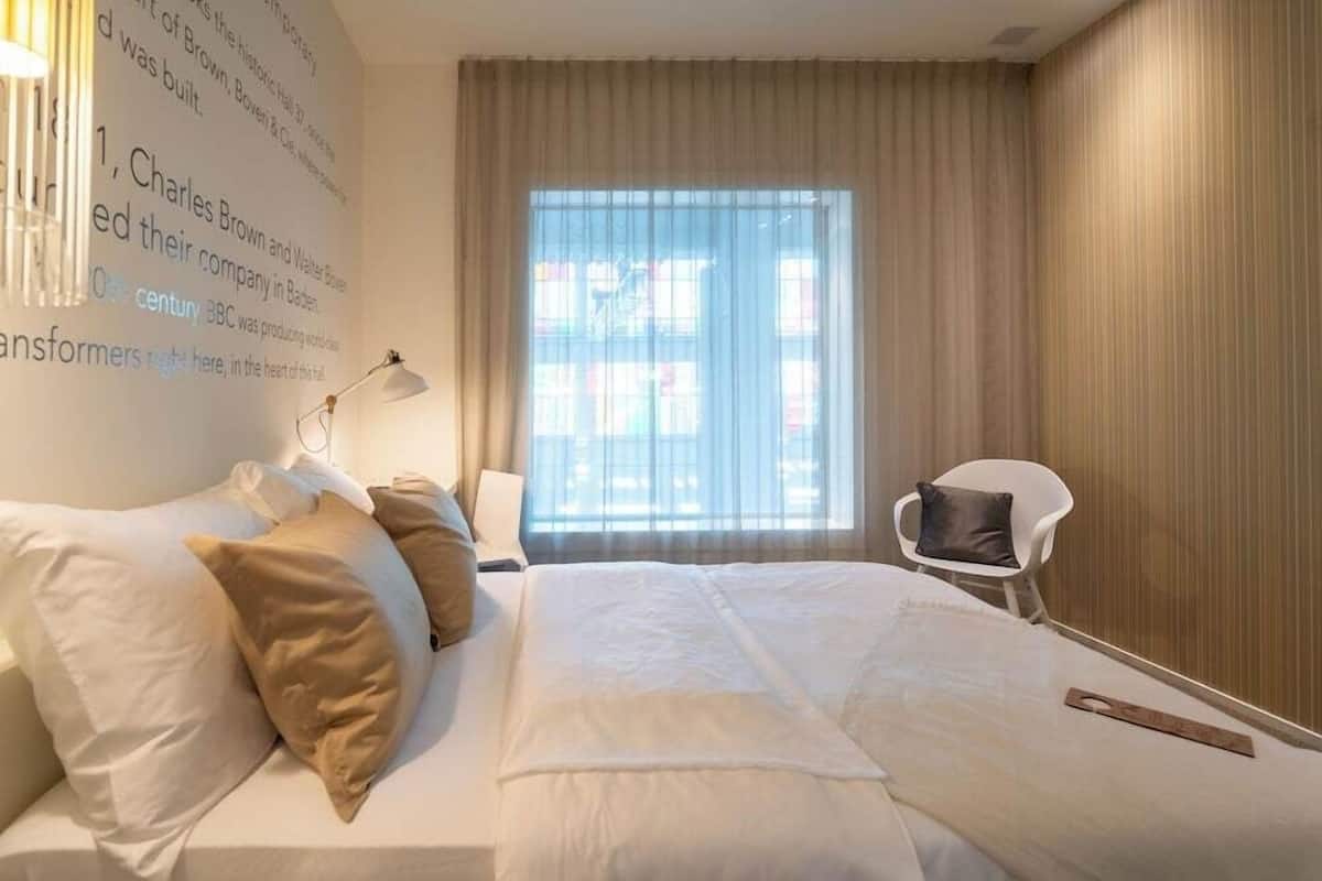 A hotel room with a large bed, a chair, a window with curtains, and a wall with text.