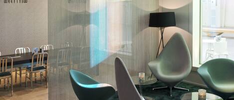 A modern interior with a dining area, a lounge with chairs, and a large window providing natural light.