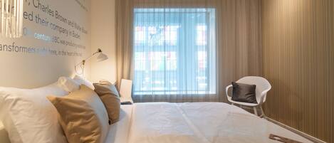 Habitación de hotel con una cama grande, una silla, un escritorio y un ventanal con cortinas.