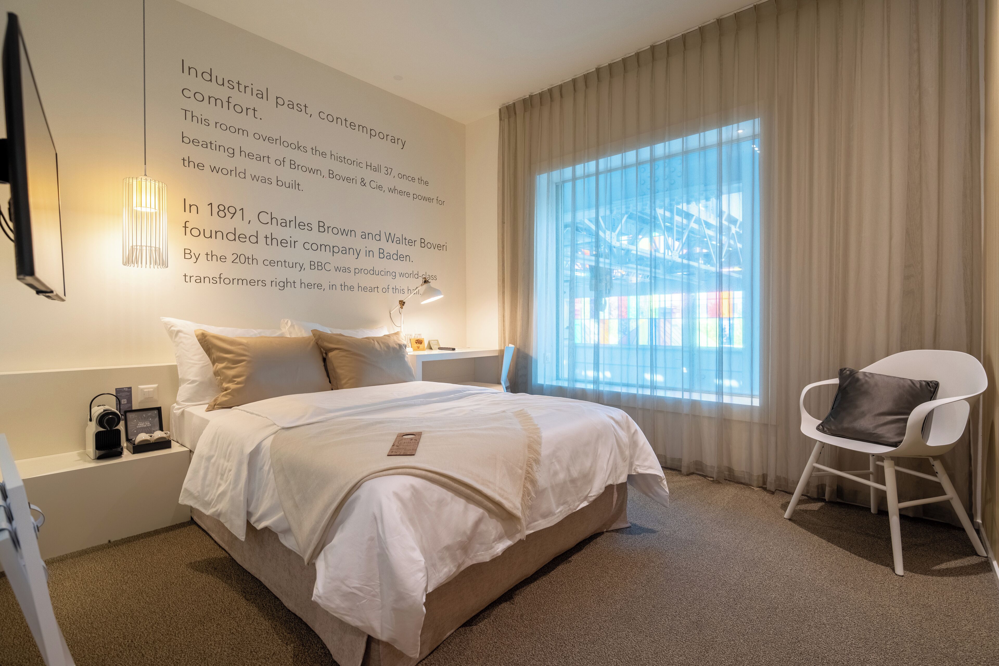 A hotel room with a large bed, a desk, a chair, and a window with curtains.