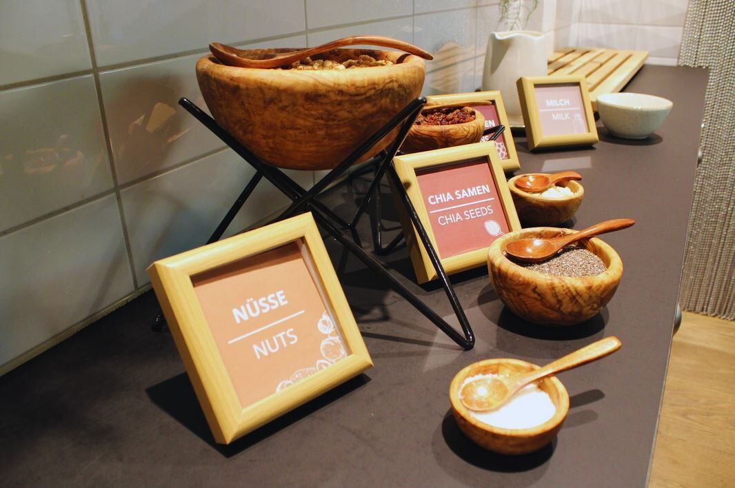Una variedad de alimentos como semillas de chía, nueces y leche, dispuestos sobre una mesa con cuencos y cucharas de madera.