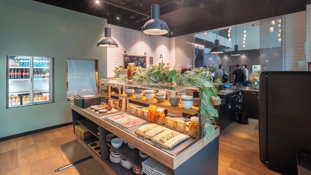 A buffet area with a variety of food items, a refrigerator, and a seating area with tables and chairs. - Trafo Hotel (Baden)