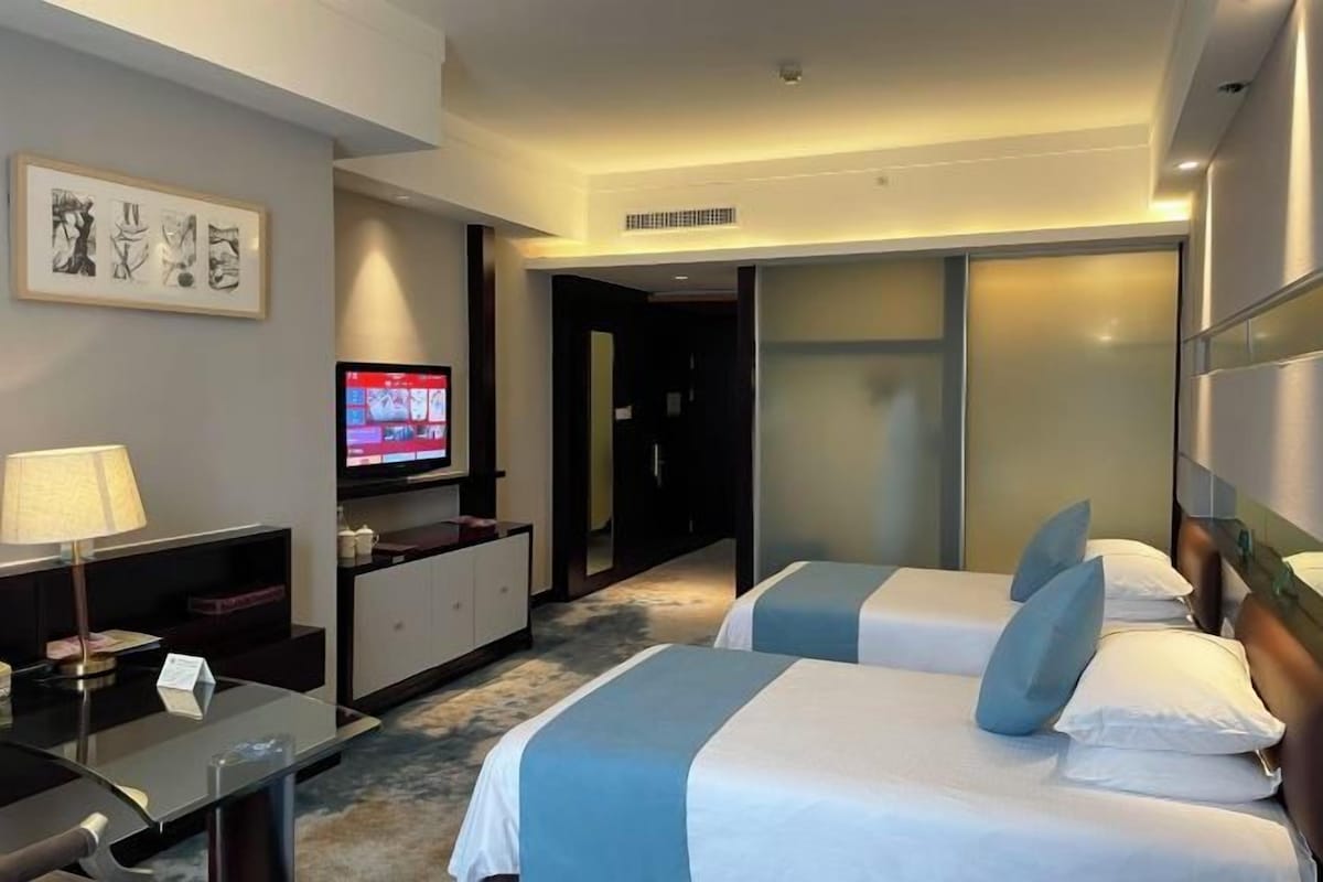 Quarto de hotel com duas camas, uma escrivaninha, televisão e obras de arte na parede.