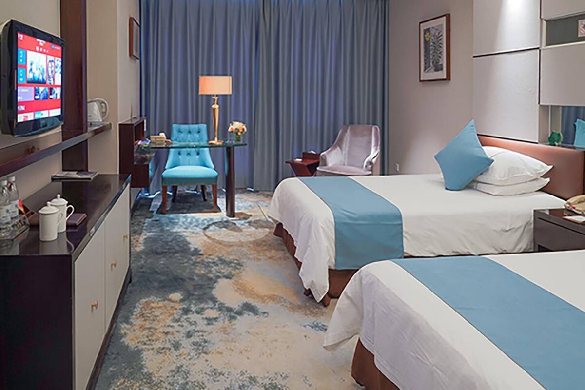 Hotellihuone, jossa on kaksi sänkyä, kirjoituspöytä lampun kanssa, televisio ja tuoli.