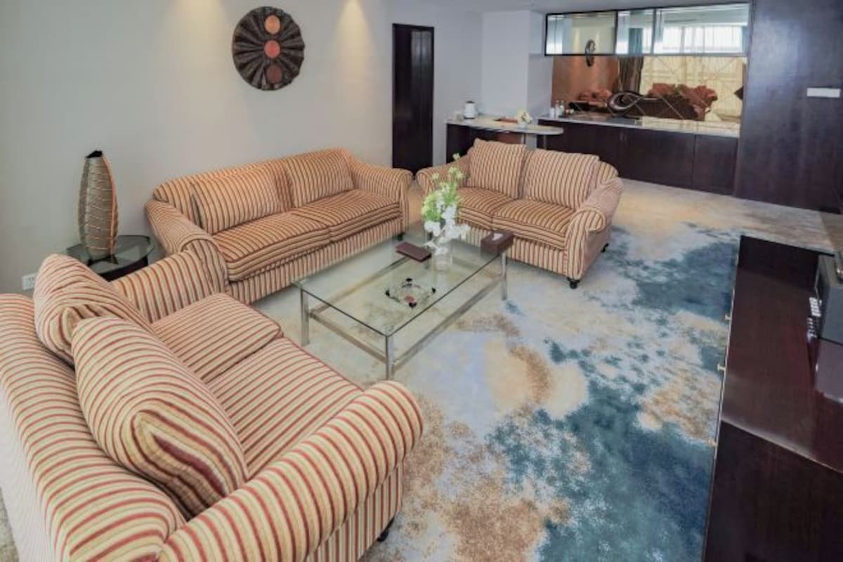 Uma sala de estar com sofás listrados, uma mesa de centro de vidro e um tapete.