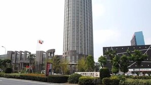 Un edificio alto y moderno con fachada curva, rodeado de otras estructuras contemporáneas y vegetación.
