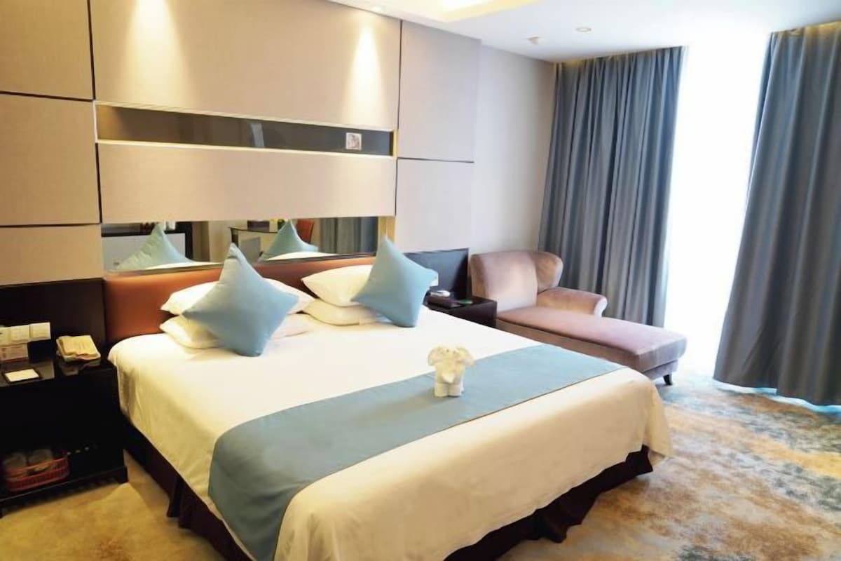 Quarto de hotel com uma cama grande, um sofá, uma mesa de cabeceira e um espelho.