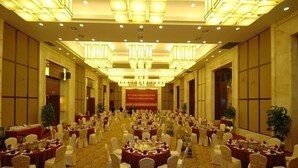 Un gran salón de banquetes con mesas redondas y sillas, una alfombra estampada y una araña.