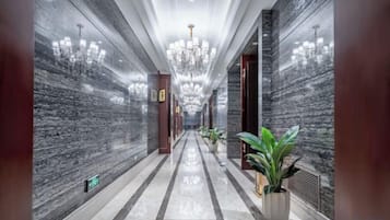 A long hallway with marble walls, a chandelier, and potted plants.