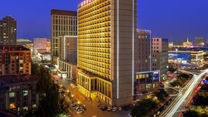 Un hotel moderno de gran altura con una fachada cuadriculada de habitaciones, rodeado por un paisaje urbano nocturno.