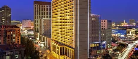 A high-rise hotel with a grid of rooms, surrounded by a cityscape at night.