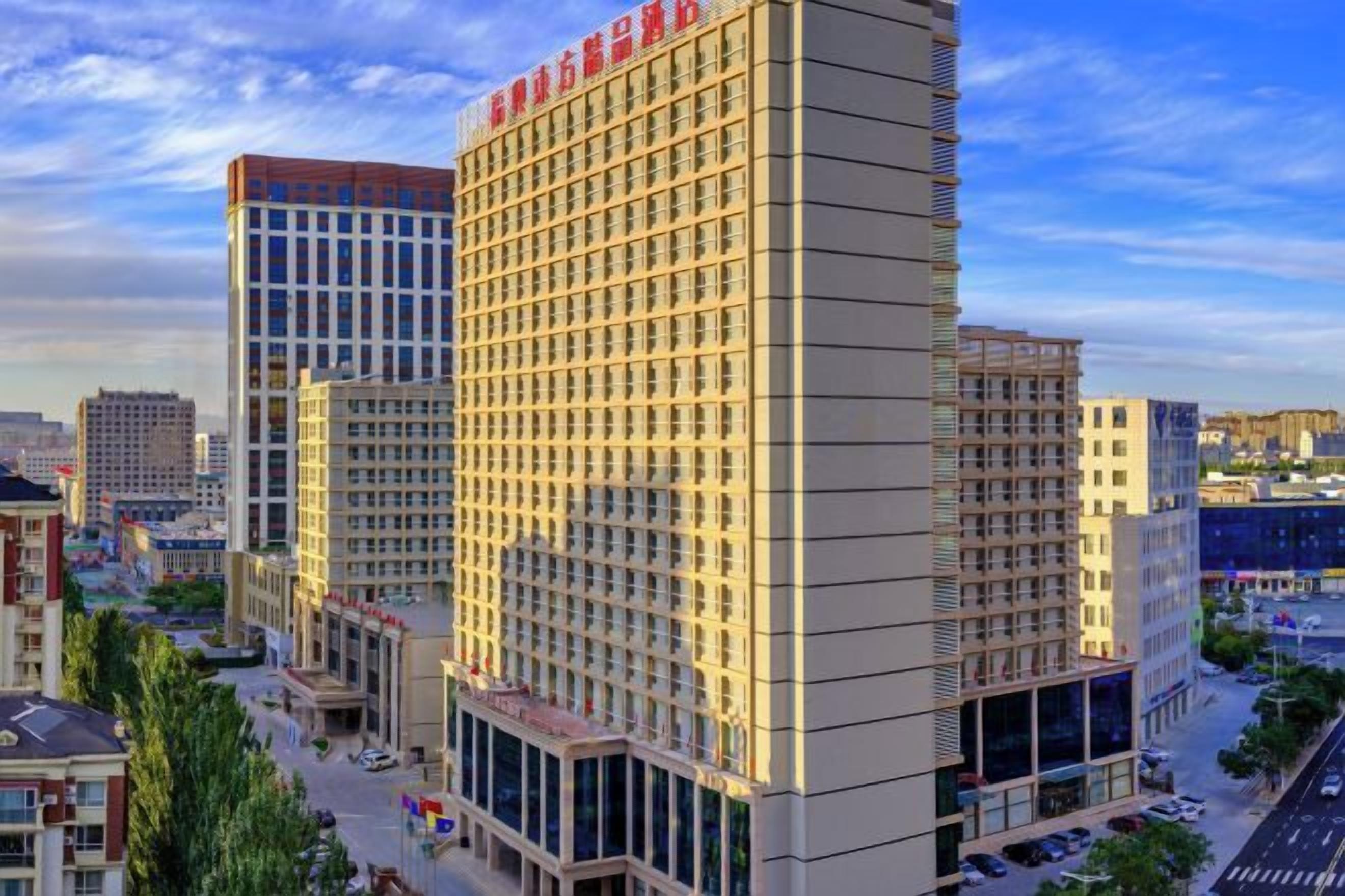 A multi-story hotel with a grid-like facade, large windows, and a prominent red sign at the top.