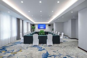 A conference room with a long table, white chairs, a large screen, and a carpeted floor. - Fuxing Oriental Boutique Hotel (Chifeng)