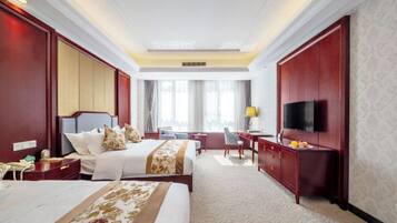 A hotel room with a large bed, a desk, a chair, a TV mounted on the wall, and a window with curtains.