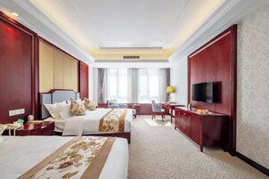Una habitación de hotel con una cama grande, un escritorio, una silla, un televisor fijado a la pared y una ventana con cortinas.