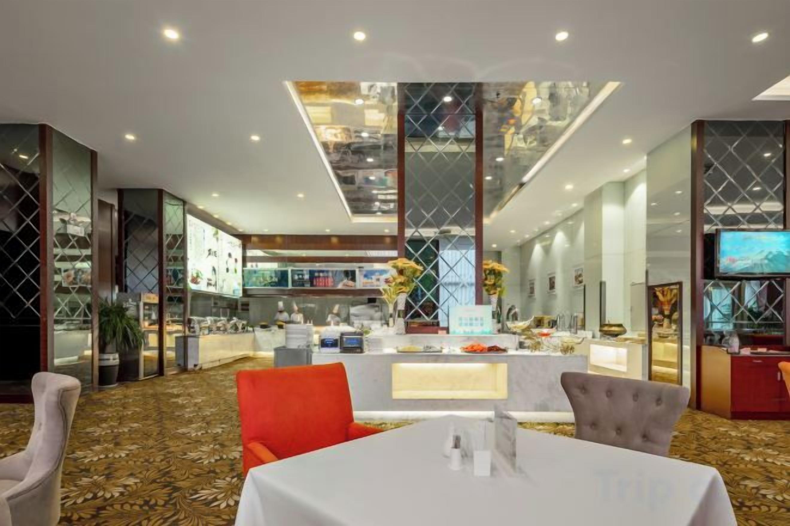 A modern hotel lobby with a central reception desk, a dining area with a white table, and a large window overlooking the interior.