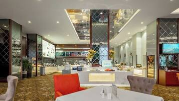 A modern hotel lobby with a central reception desk, a dining area with a white table, and a large window overlooking the interior.
