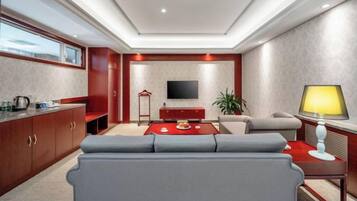 Una sala moderna con un sofá, una mesa de centro roja, un televisor y una lámpara.