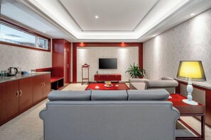 A modern living room with a sofa, a red coffee table, a TV, and a lamp. - Fuxing Oriental Boutique Hotel (Chifeng)