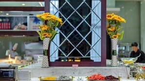 Zona de recepción de un hotel con un mostrador de mármol, dos jarrones de girasoles y una celosía decorativa en la ventana.