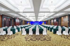Ein Konferenzraum mit Reihen weißer Stühle, einer Bühne mit blauem Hintergrund und Kristallleuchtern.