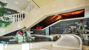 Un área de piscina interior moderna con una cascada de piedra, una escalera y vistas al cielo.