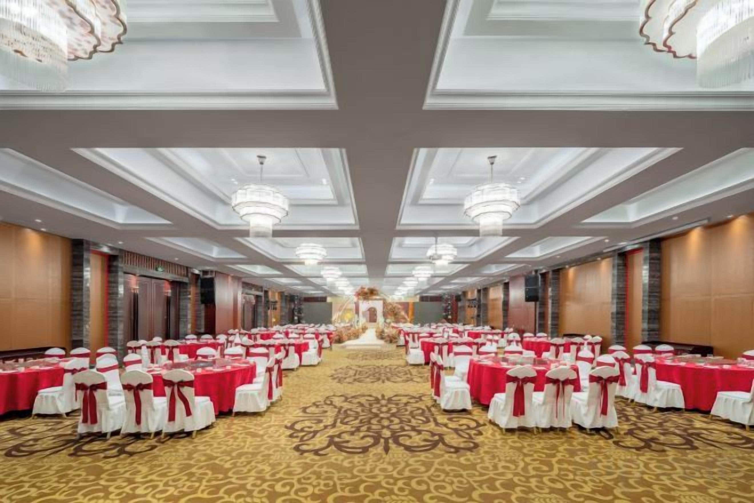 Une salle de banquet avec des rangées de tables, des lustres et un sol recouvert de moquette.
