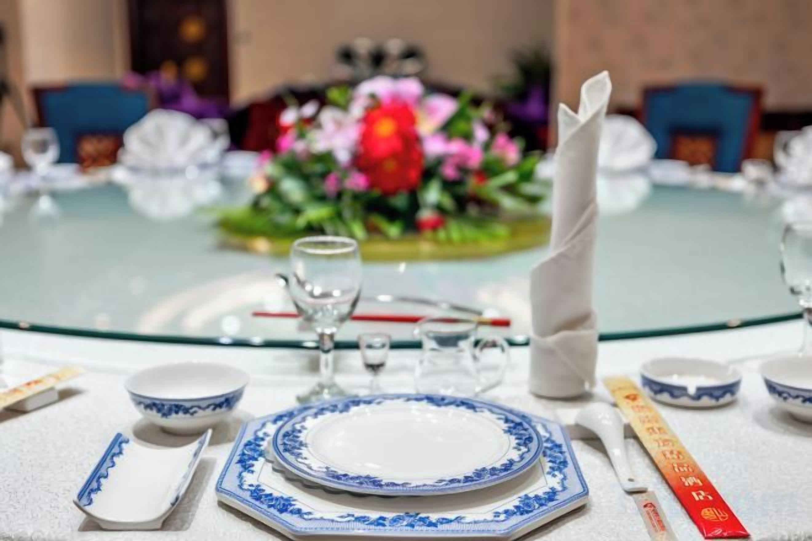 A round dining table with a glass top, white tablecloth, and blue and white patterned plates.